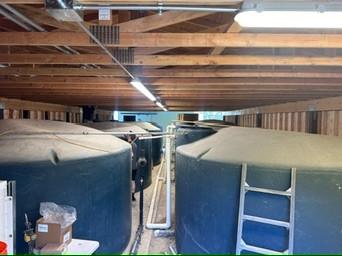Row of large water storage tanks under a wood-framed roof