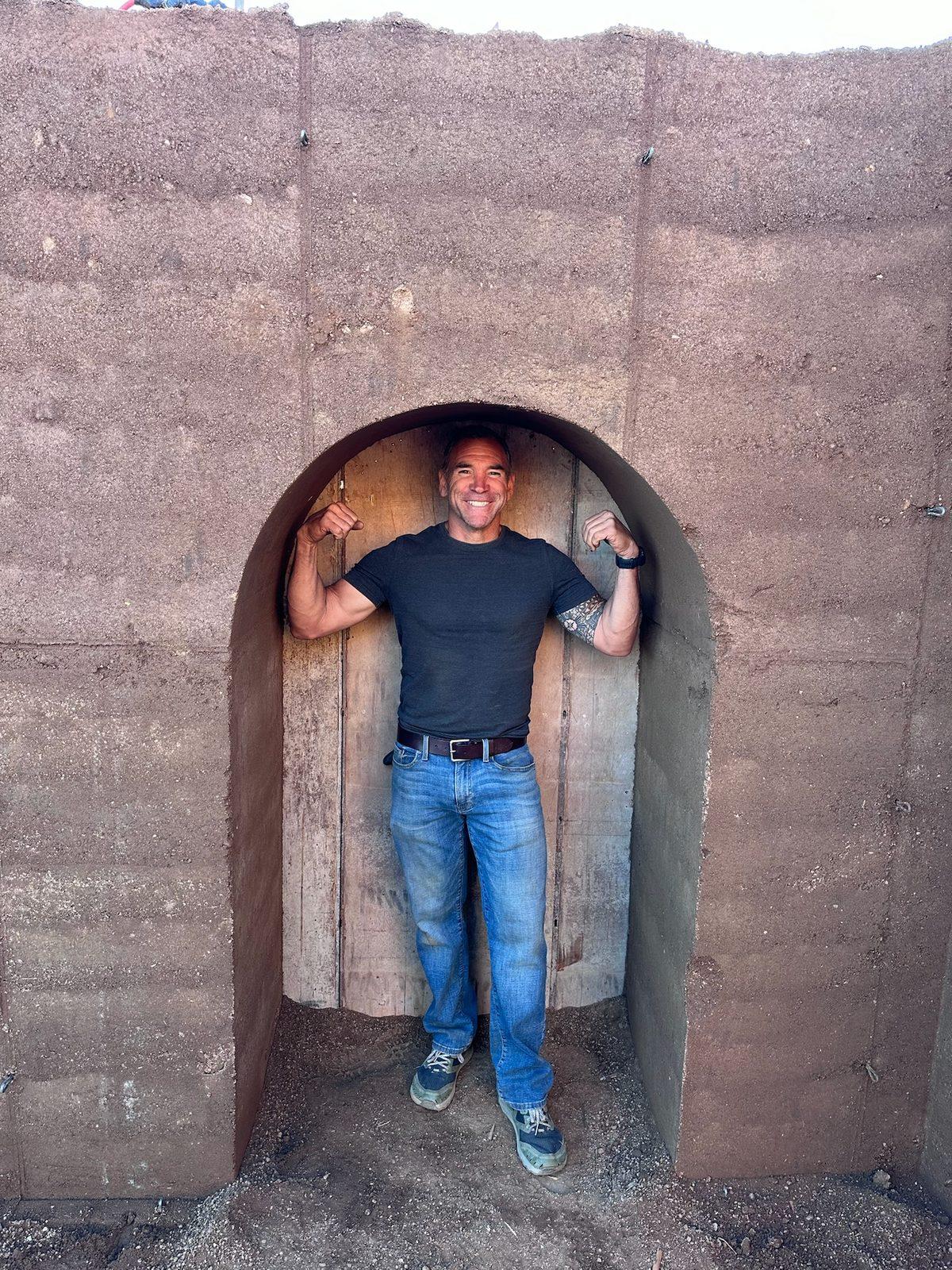 Brian Johnson standing in an arched doorway cut through a cured rammed-earth wall