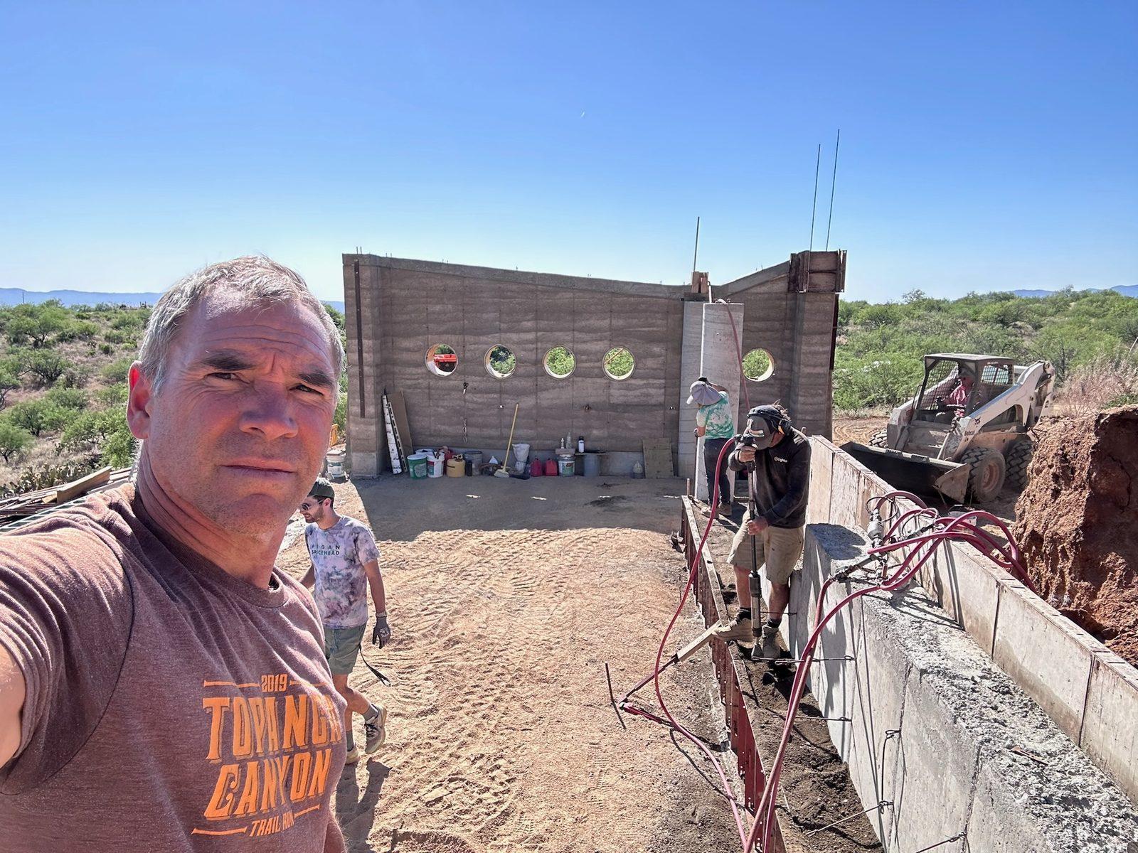 Brian Johnson on the job site in front of a rammed-earth wall form with round window forms
