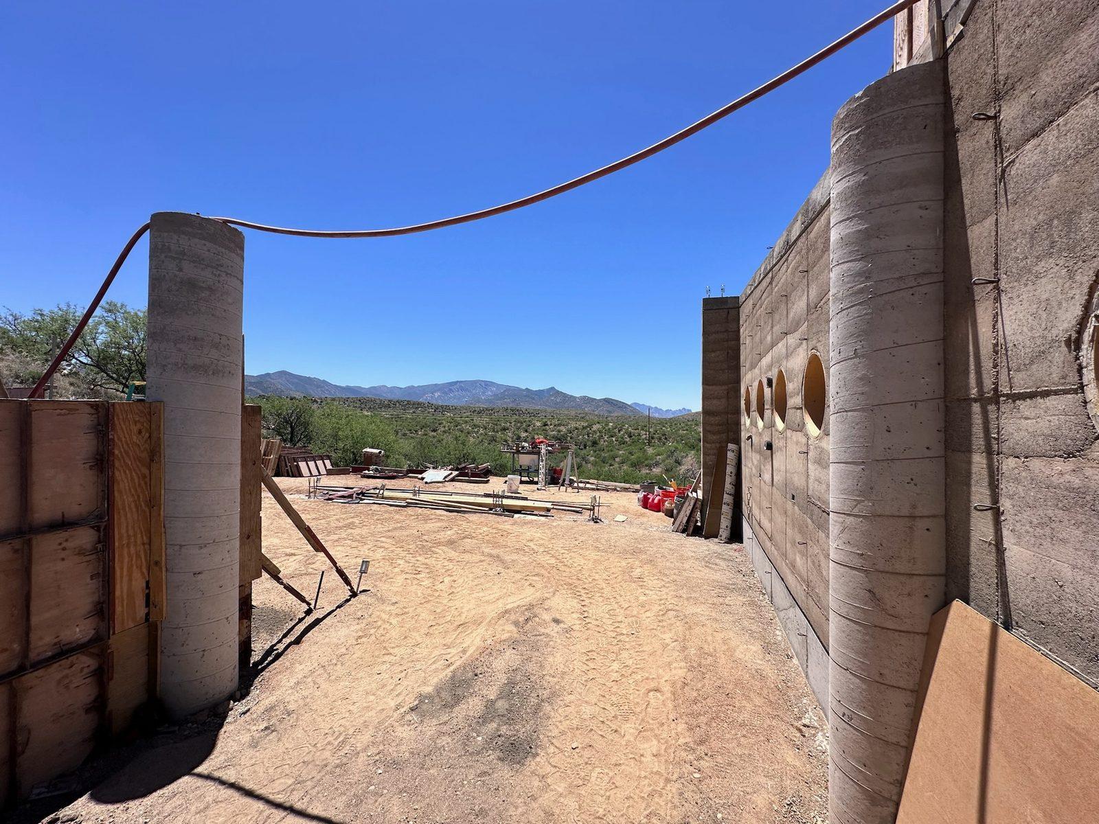 Stripped rammed-earth walls with round openings and a tall rammed-earth column
