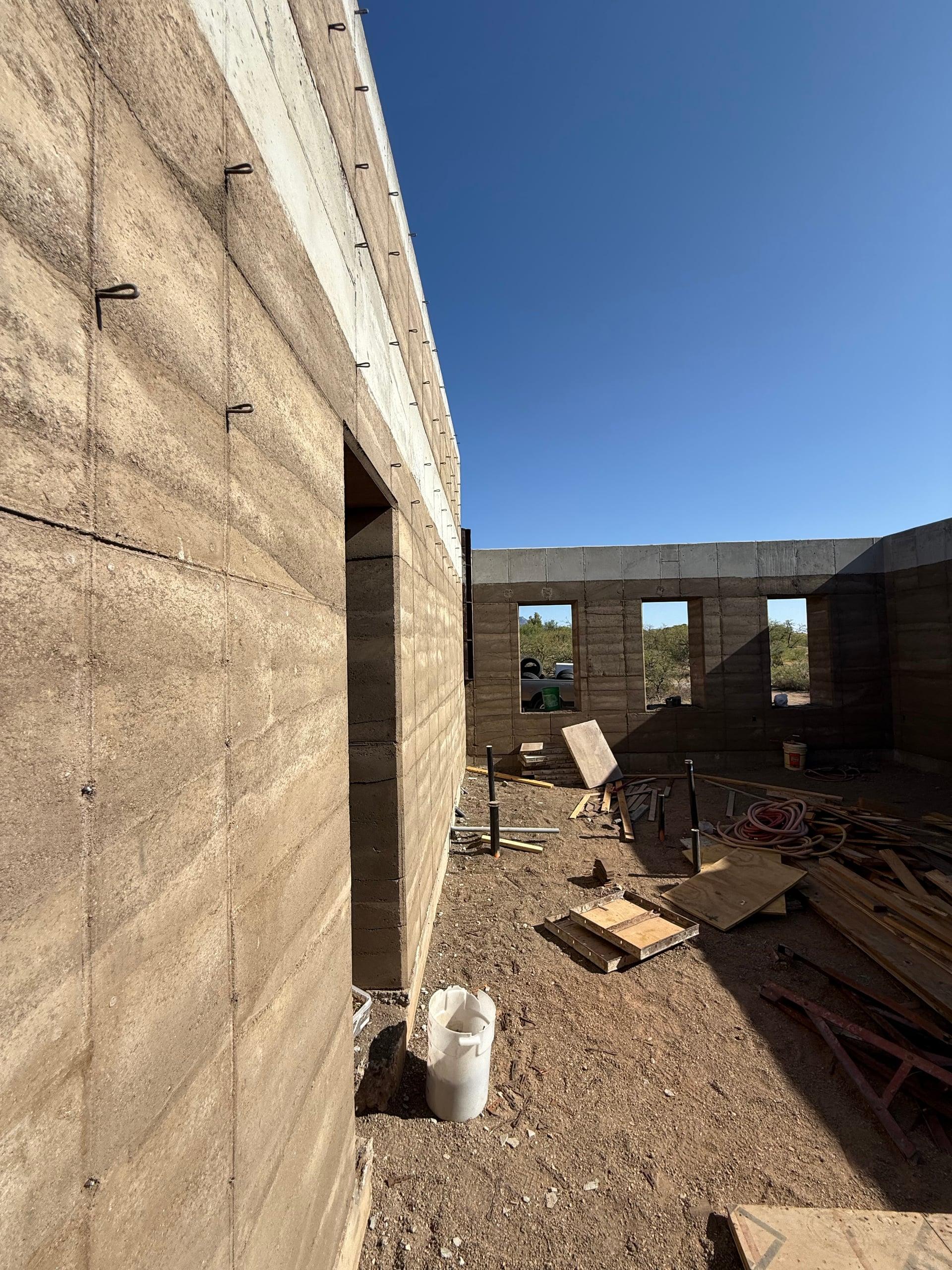 Cured rammed-earth walls with door and window openings, June 2025