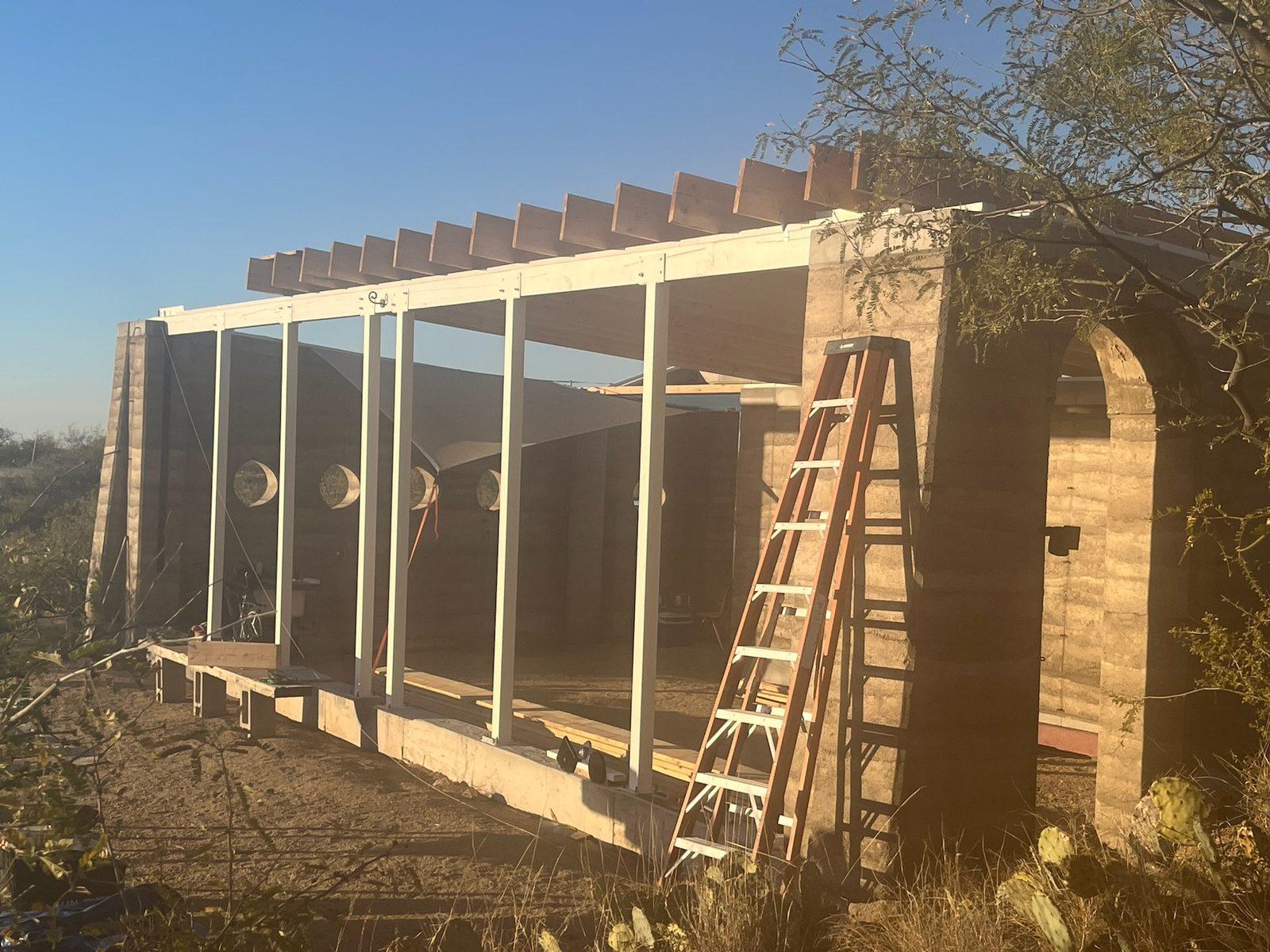 Rammed-earth walls with an arched opening and the roof framing going up