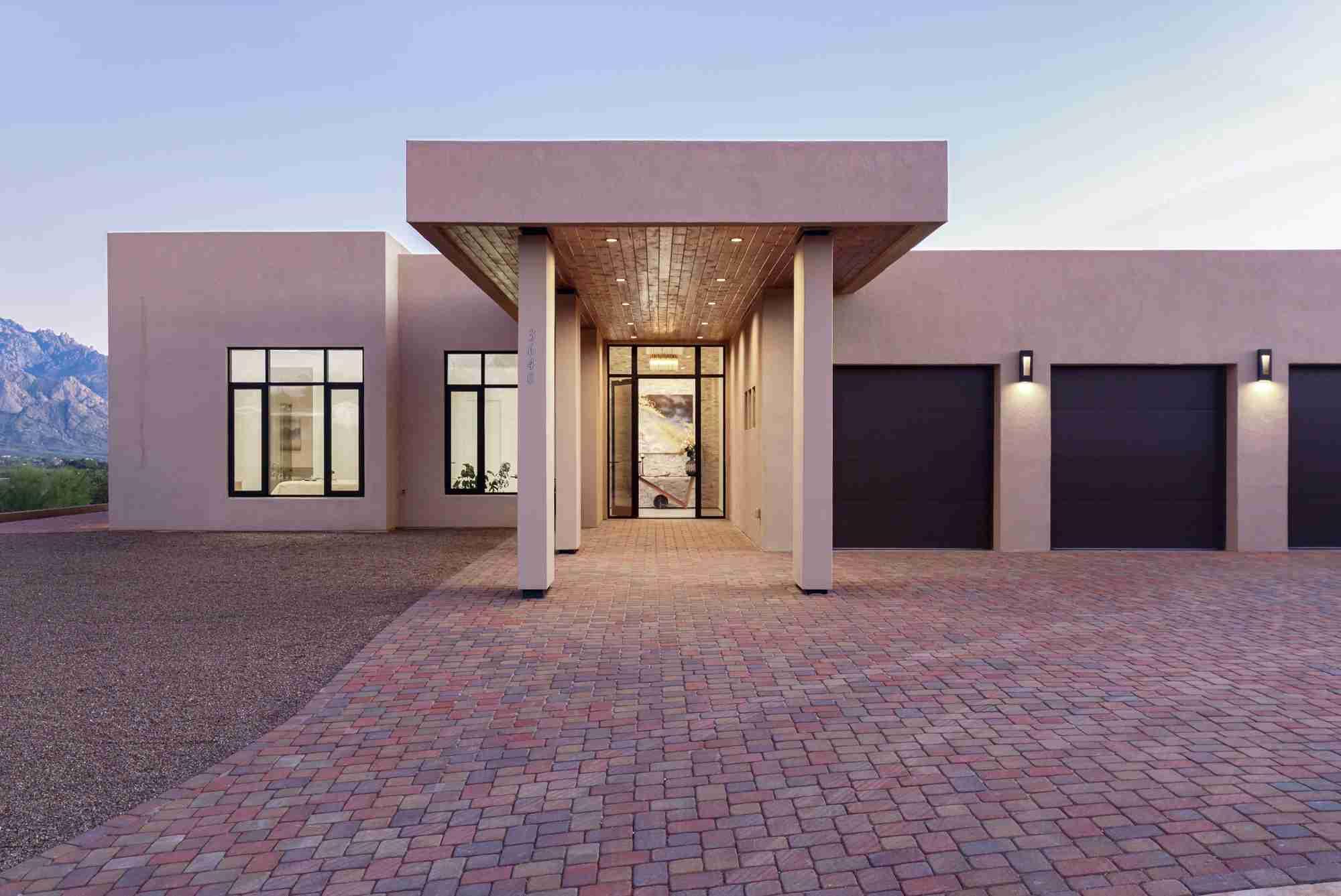 The Sanctuary House at dusk: covered entry walk, paver drive, and mountain backdrop