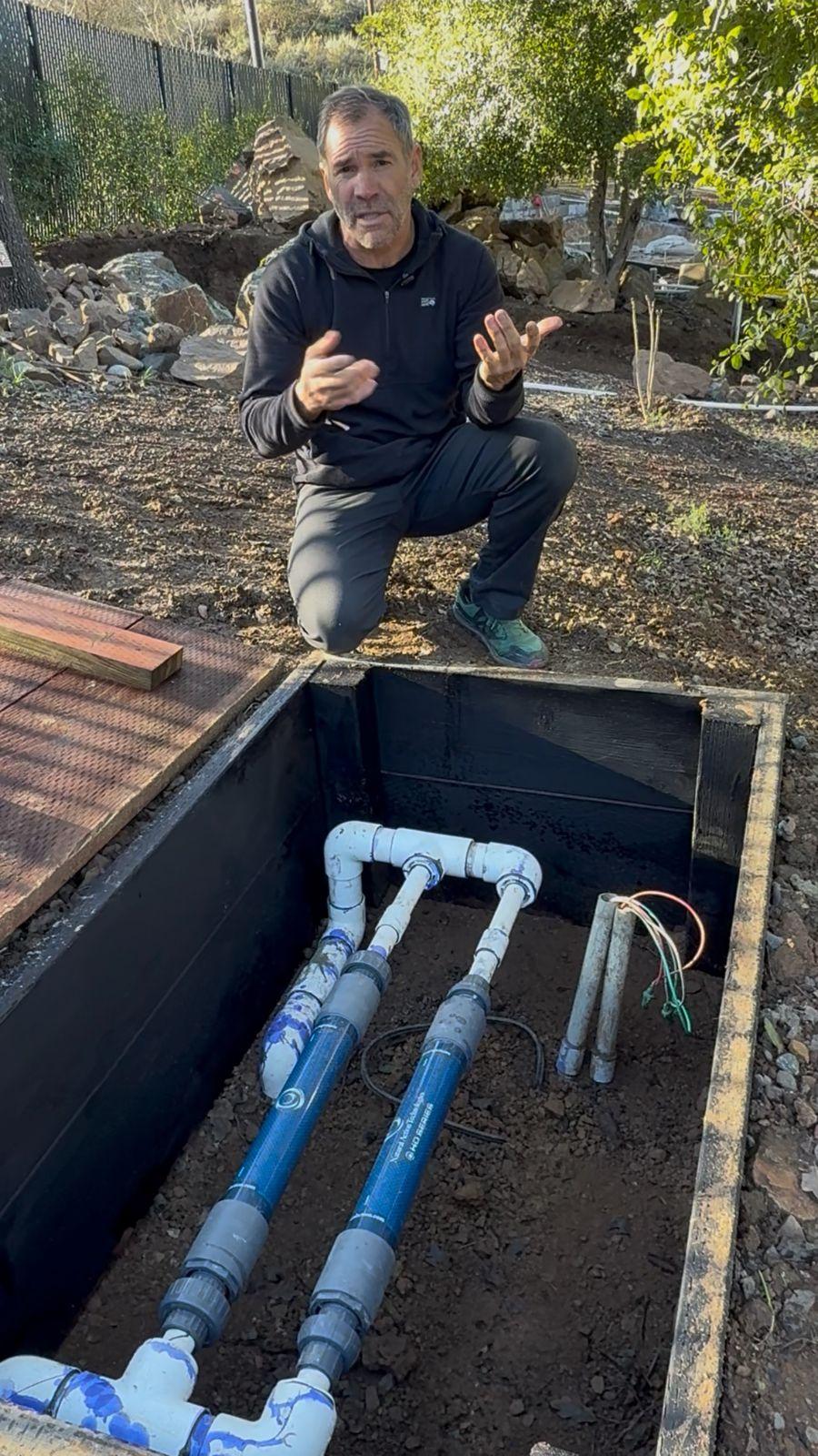 Brian Johnson kneeling beside an open box housing inline structured water units on the buried supply line