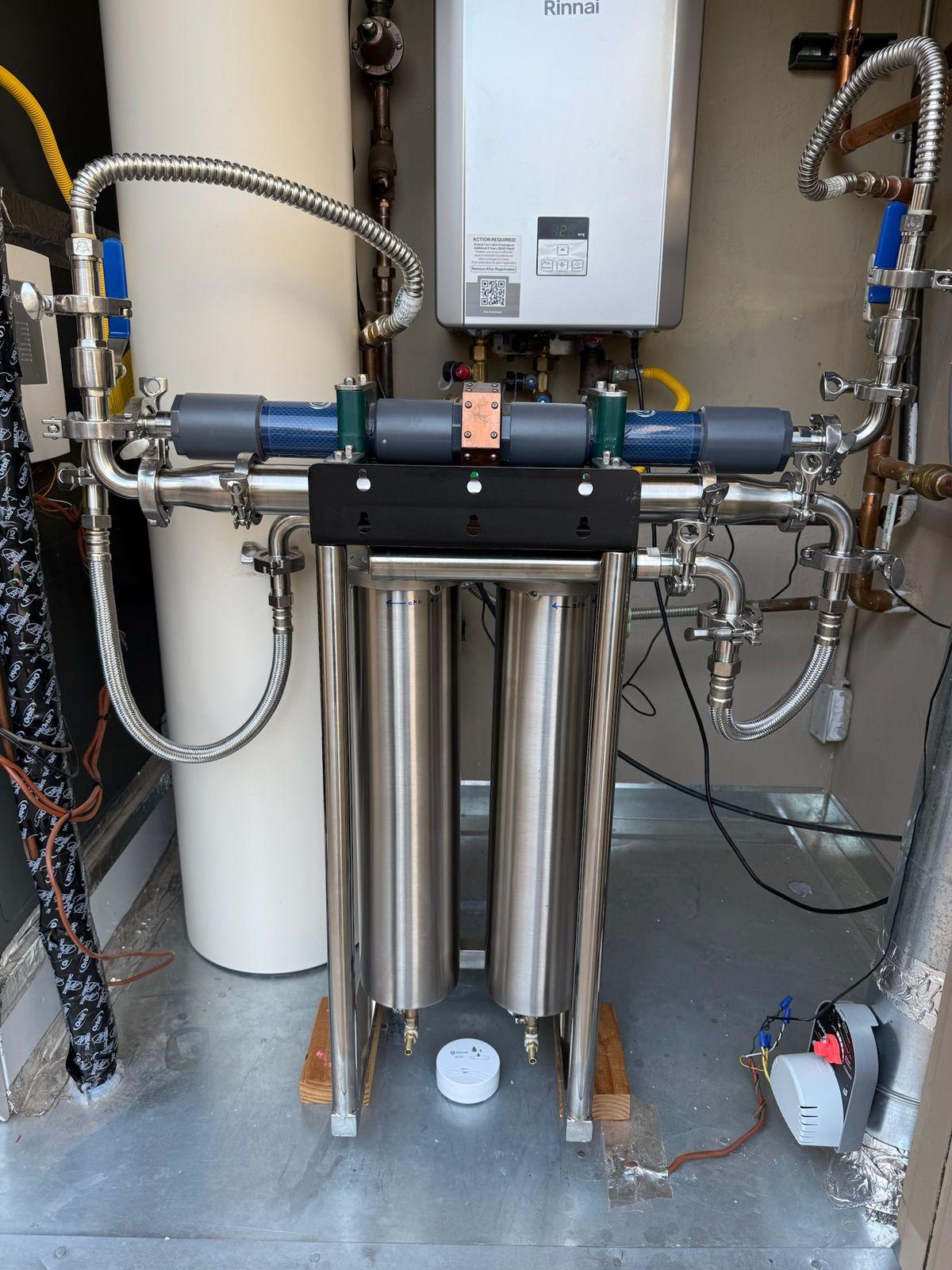 Stainless two-housing water system with inline units plumbed into a utility closet next to a tankless heater