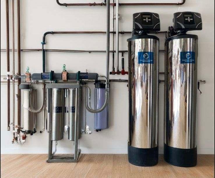 Stainless whole-home water system on a wall beside two tall treatment tanks