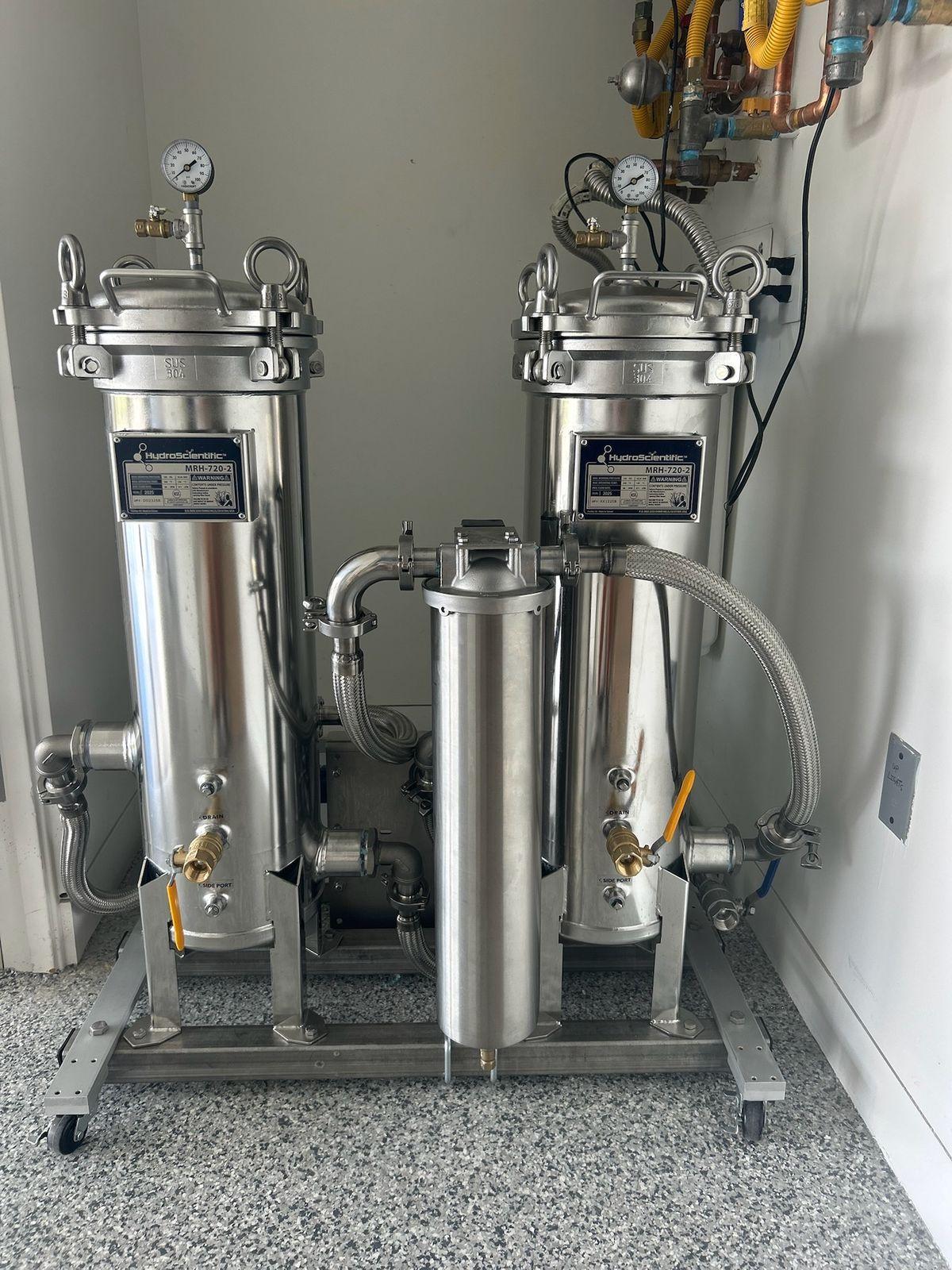 Stainless two-vessel water system with a center housing on a rolling base against a white wall