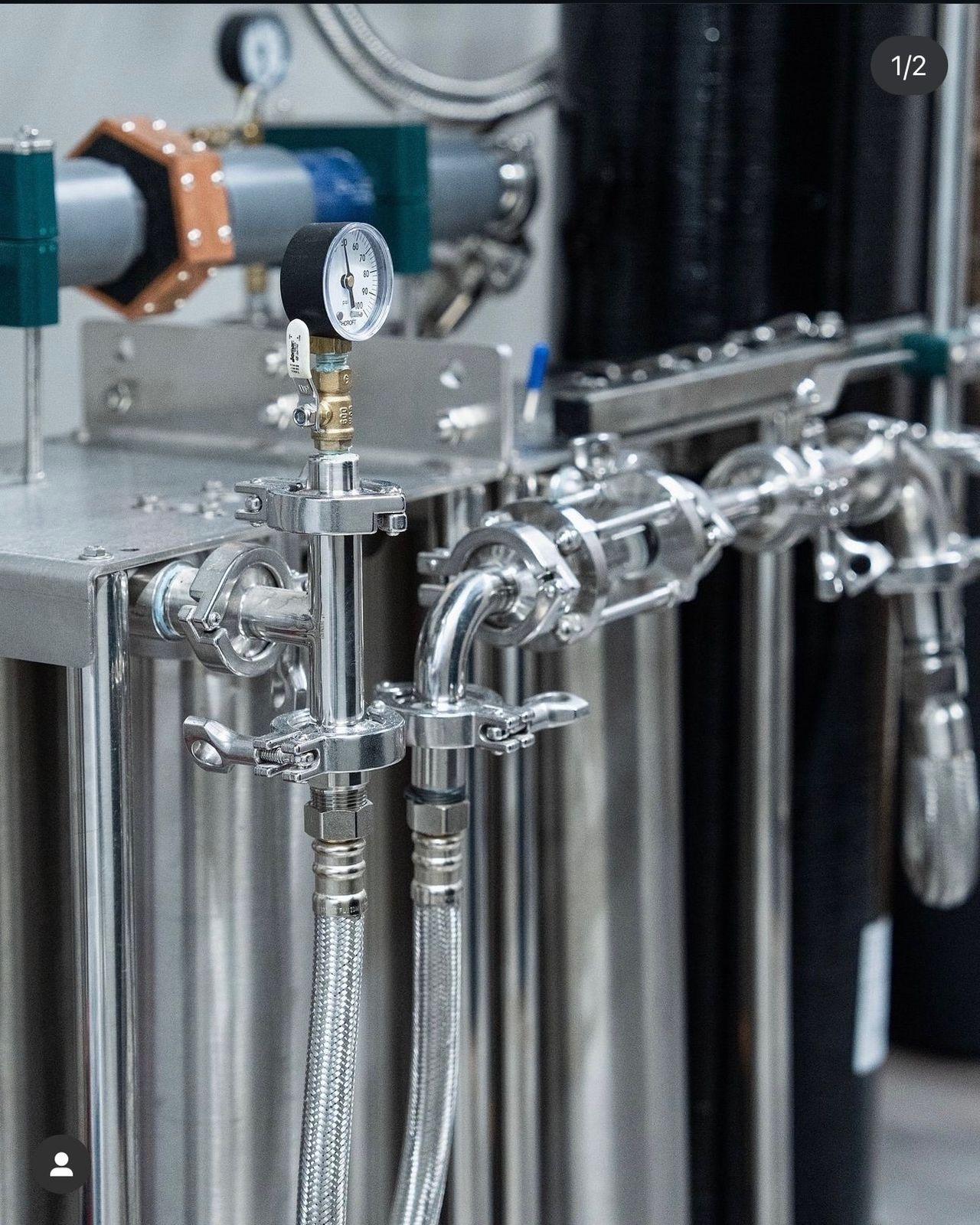 Close-up of tri-clamp sanitary fittings, a pressure gauge, and stainless piping