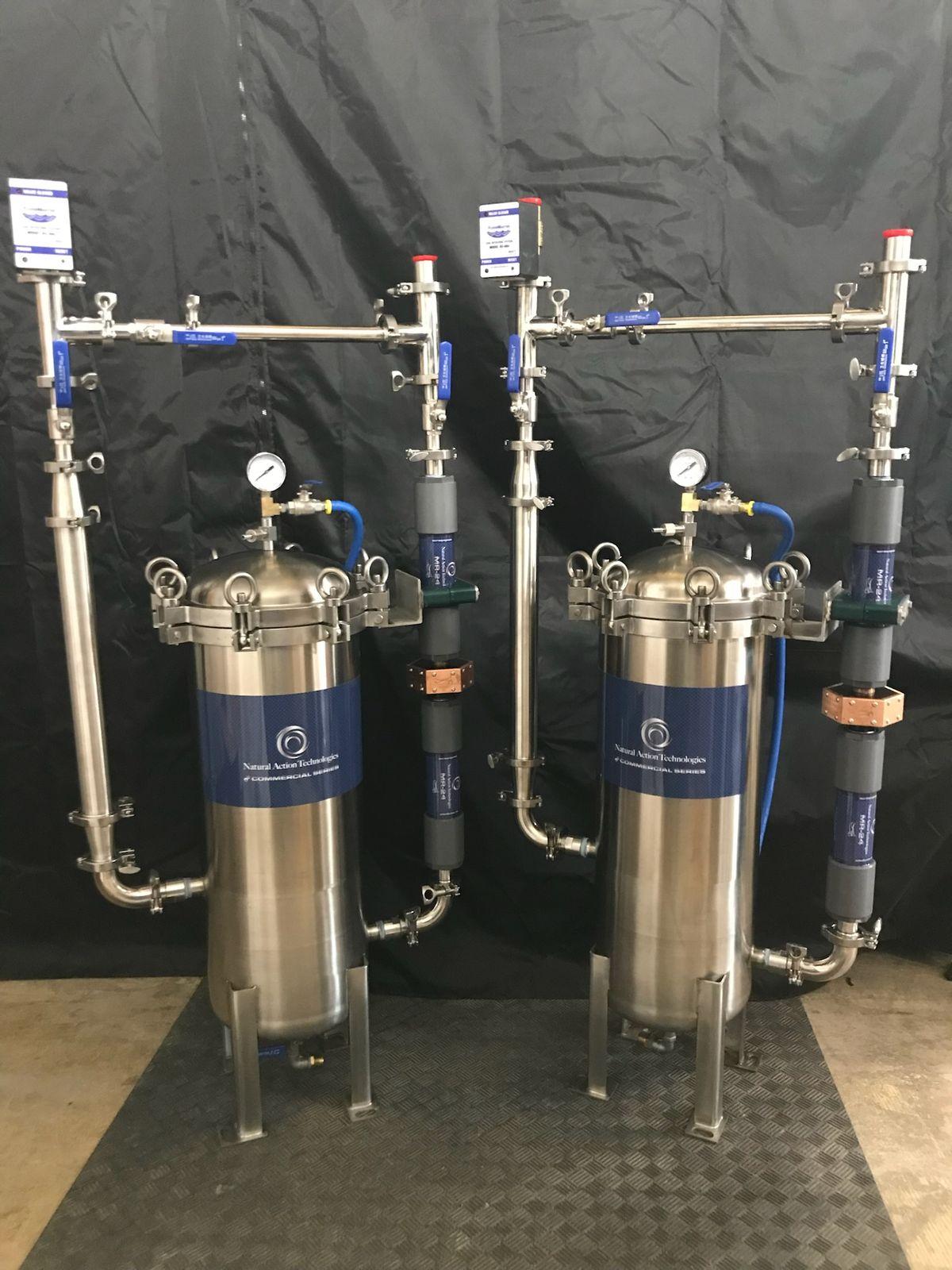 Two stainless whole-home water assemblies standing side by side in the shop