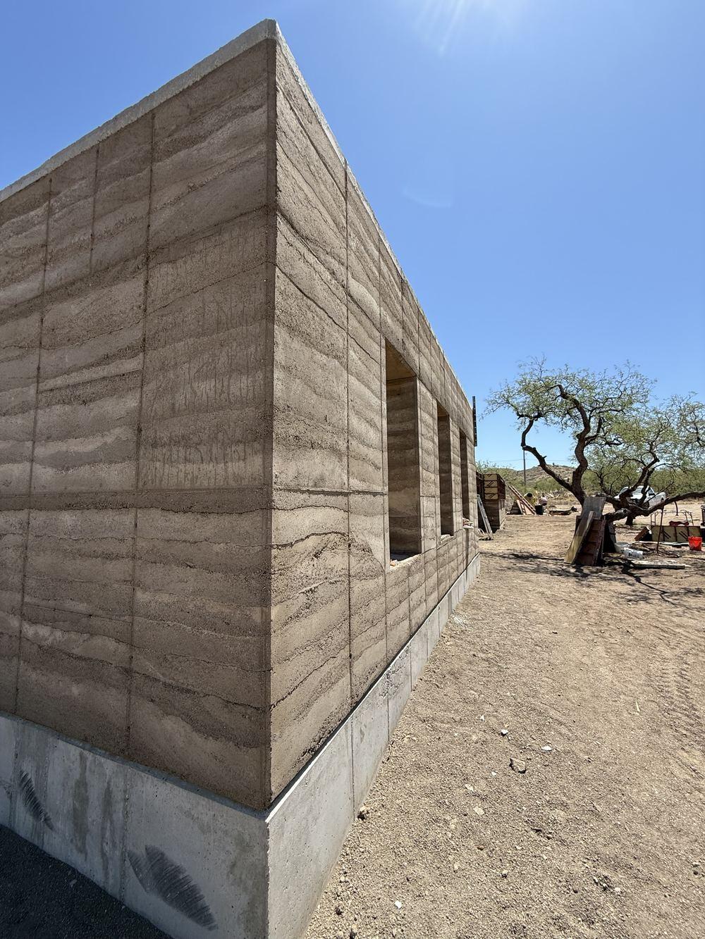 Long cured rammed-earth elevation with window openings cut through