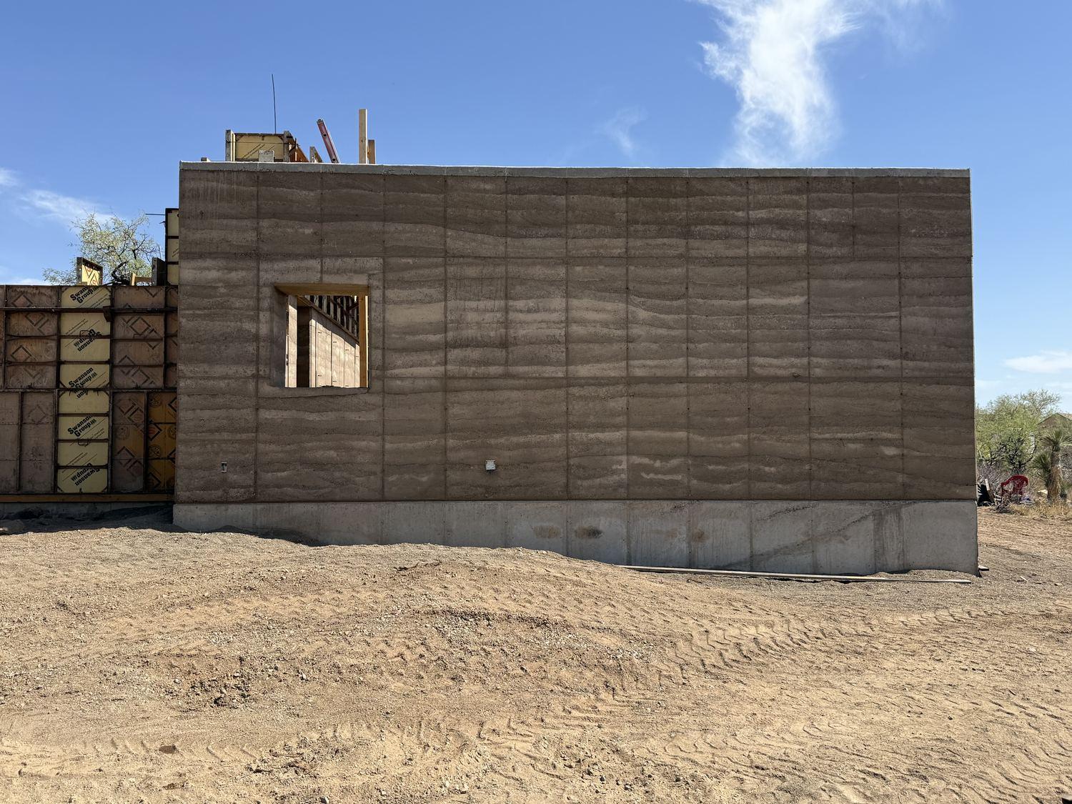 Cured rammed-earth wall with a square window opening framing the desert