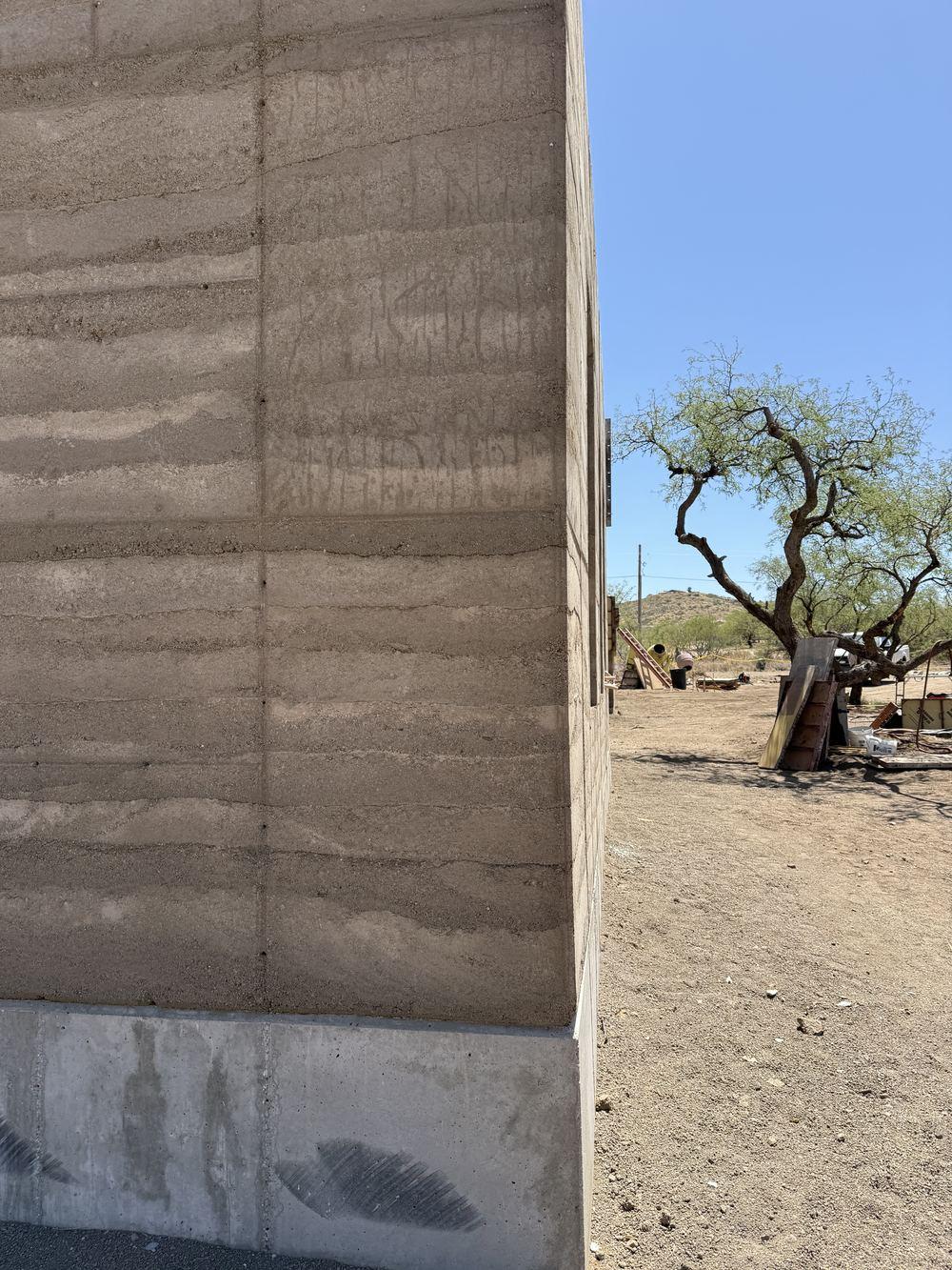 Tall cured rammed-earth wall showing horizontal lift striations