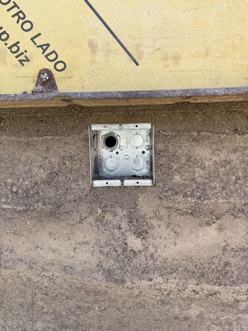 Electrical box cast flush into the face of a cured rammed-earth wall