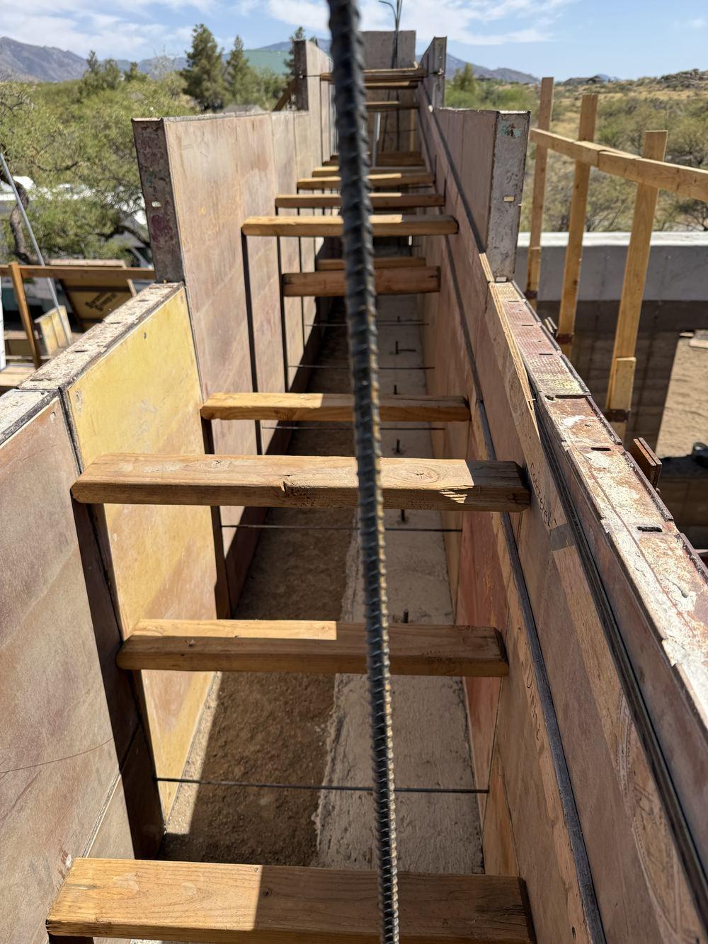 Rebar cage running the length of an open rammed-earth formwork channel