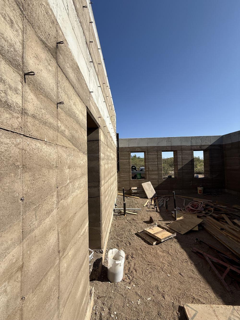 Interior of the rammed-earth shell looking out through a wall opening to the desert