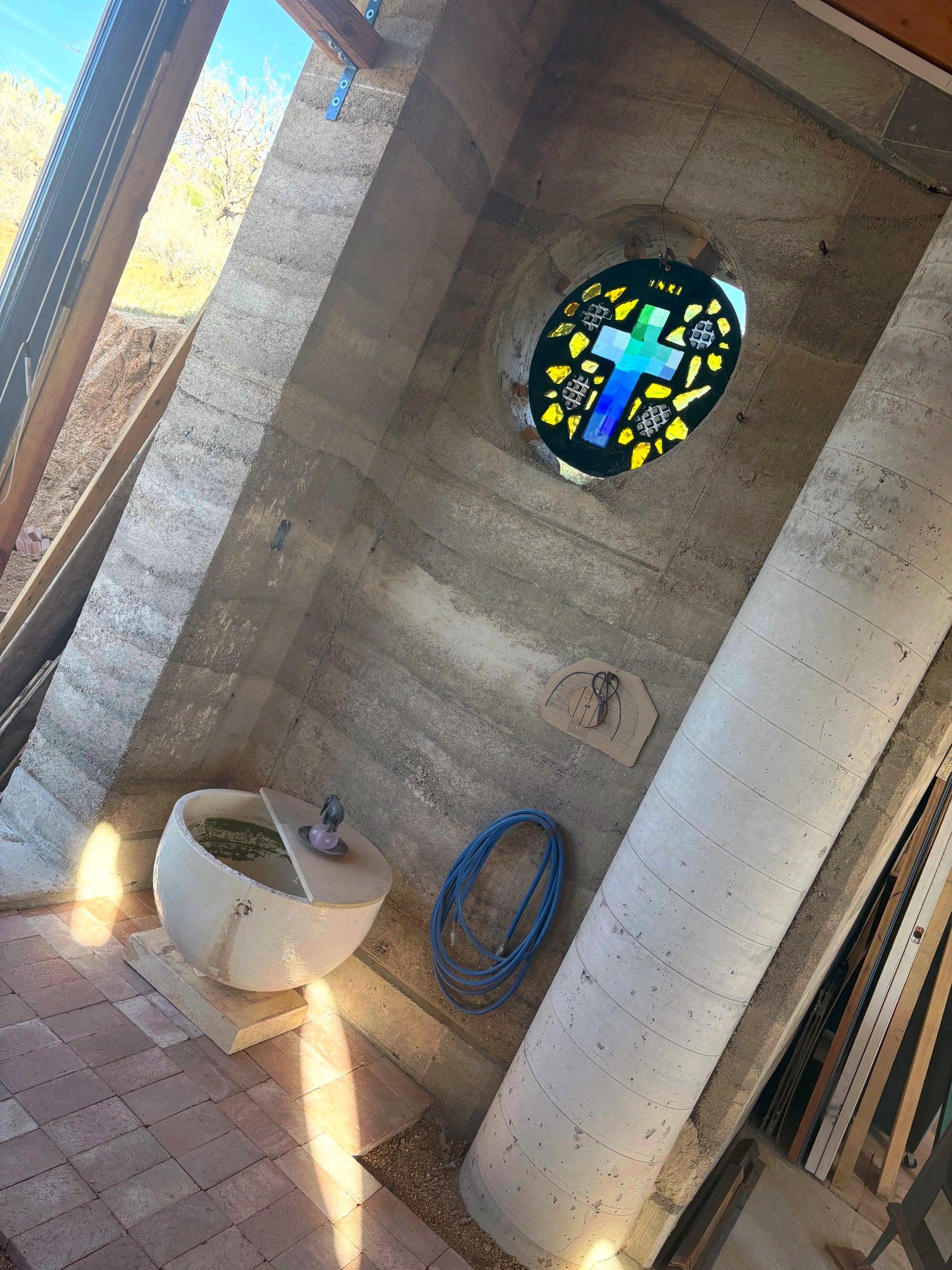 Interior with stained-glass cross window in cured rammed-earth wall