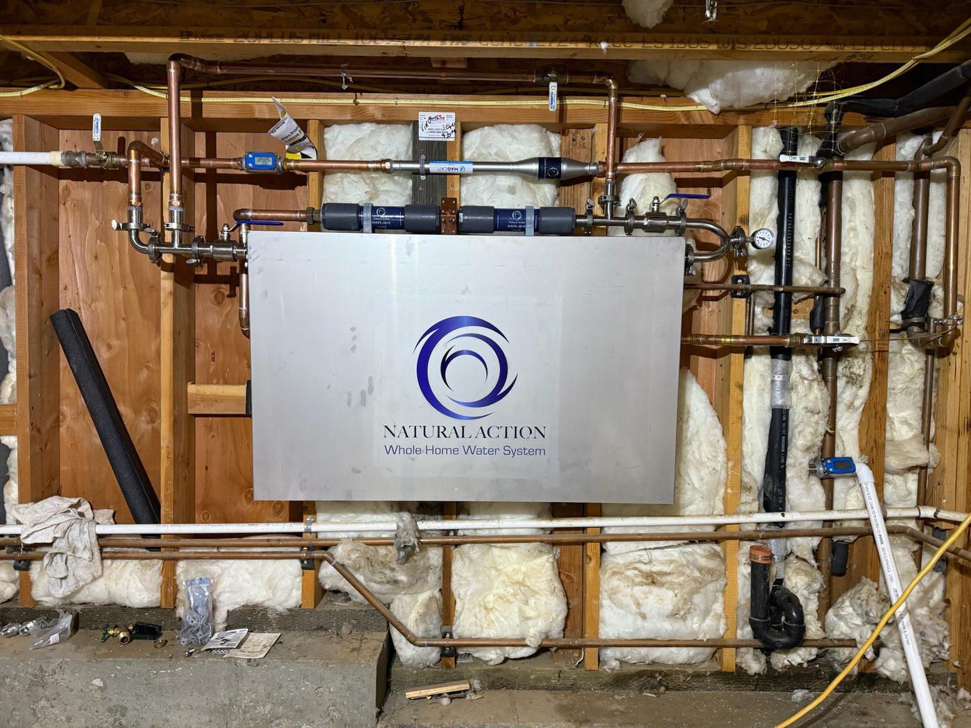 Stainless Natural Action Whole Home Water System cover installed over the cartridge bank on a framed utility wall
