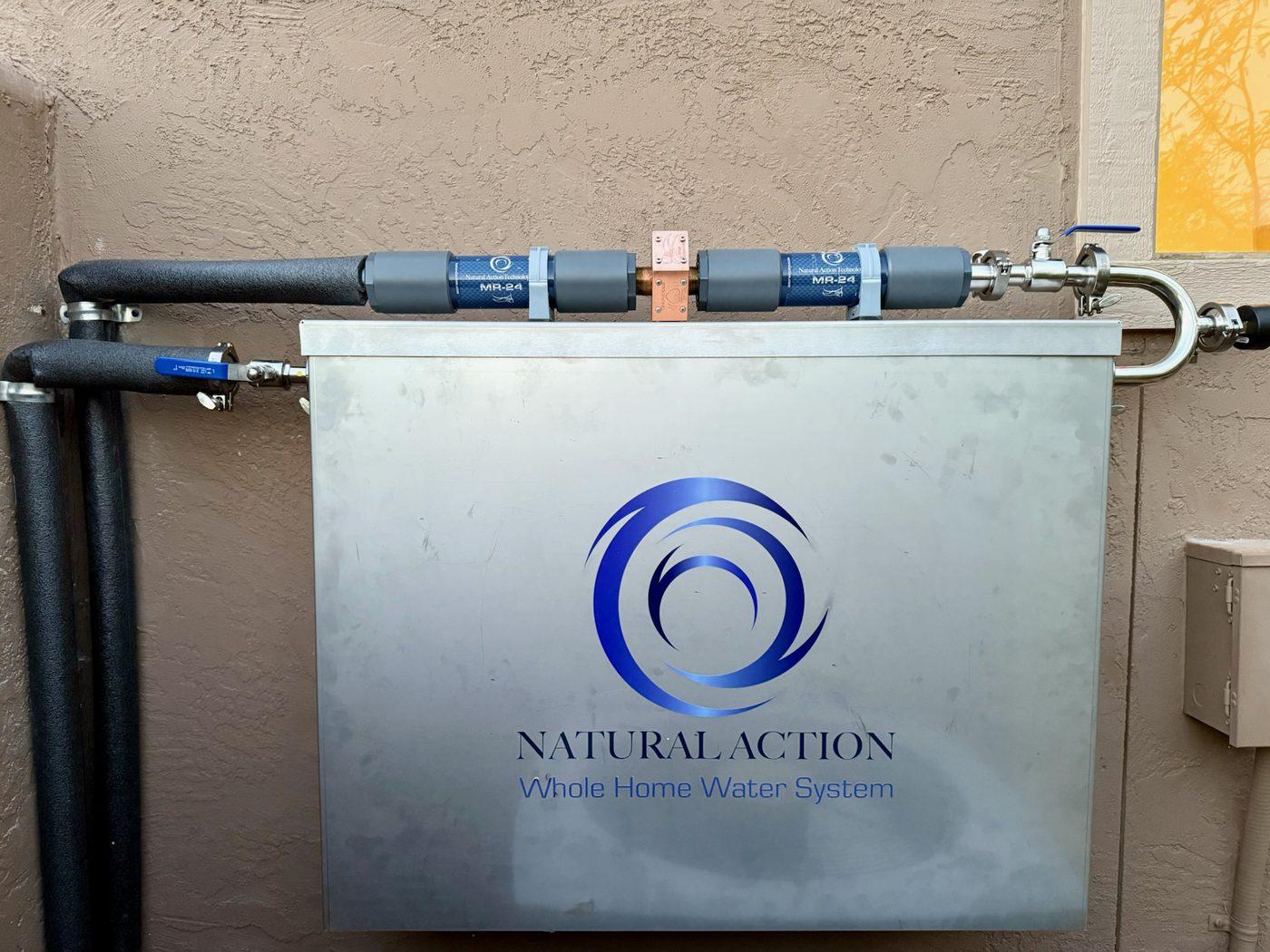 Weather enclosure on an exterior stucco wall with two MR-24 inline structured-water units and insulated supply lines above it