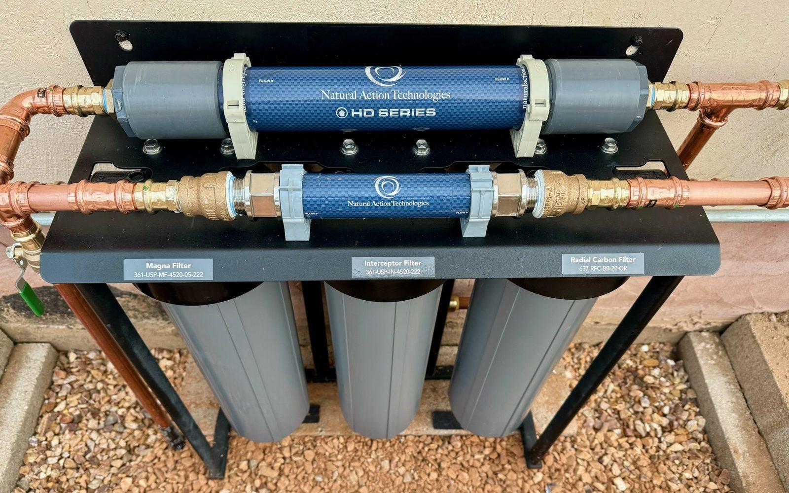 Natural Action Technologies HD Series structured-water units on a labeled three-stage filter manifold, plumbed in copper against an exterior wall