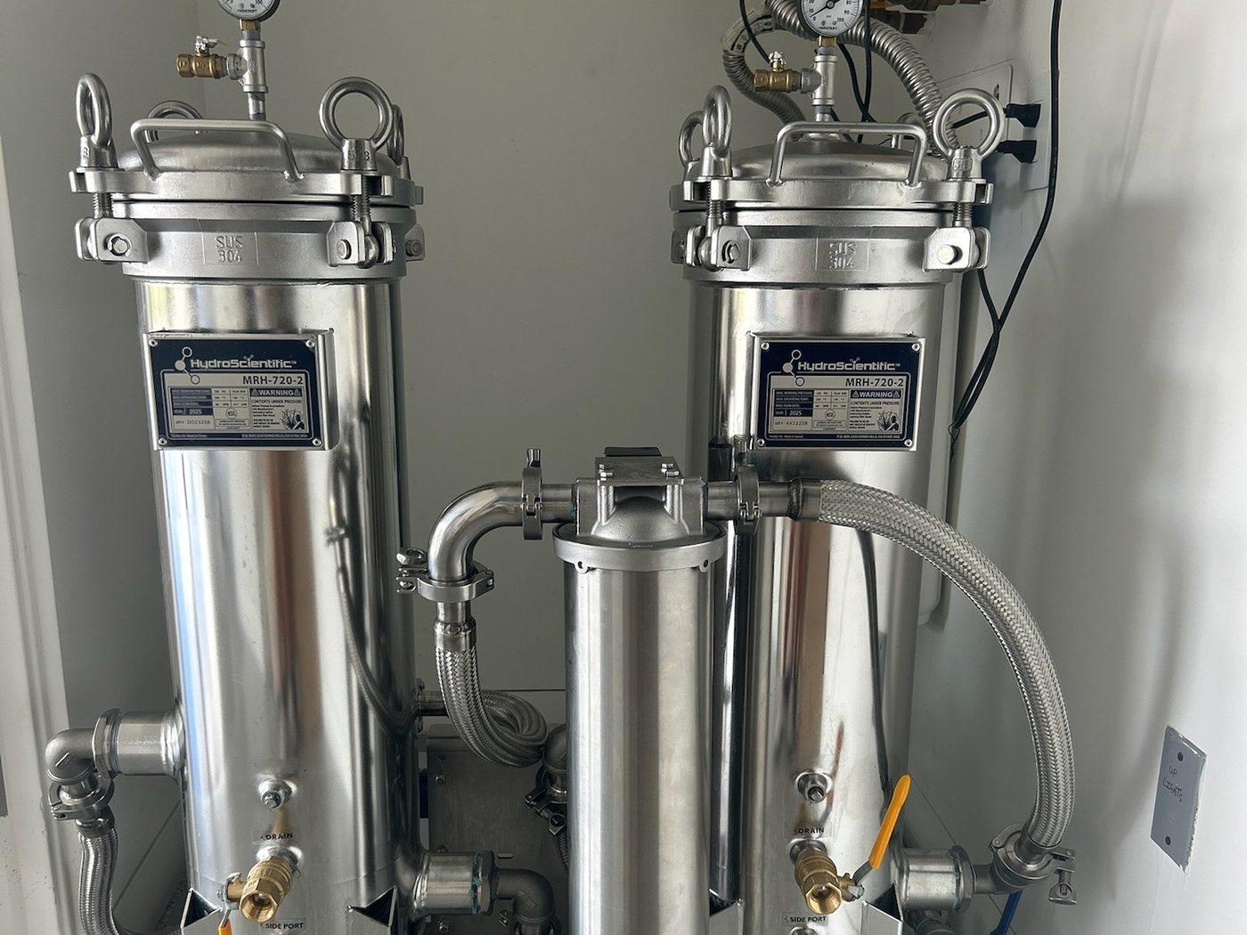 Two stainless filter housings with pressure gauges on a rolling stainless frame in a finished mechanical room
