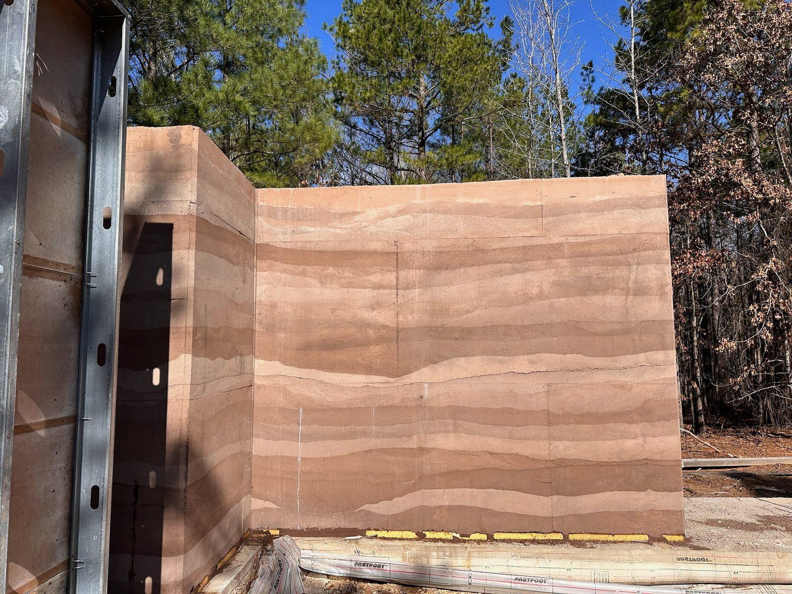 Tall rammed earth wall panel in a wooded clearing