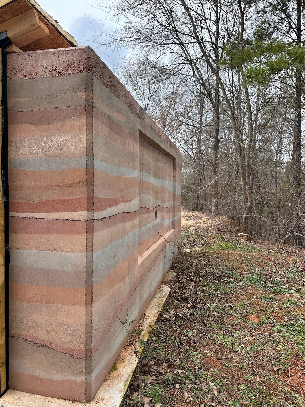 Long rammed earth wall along a wooded path