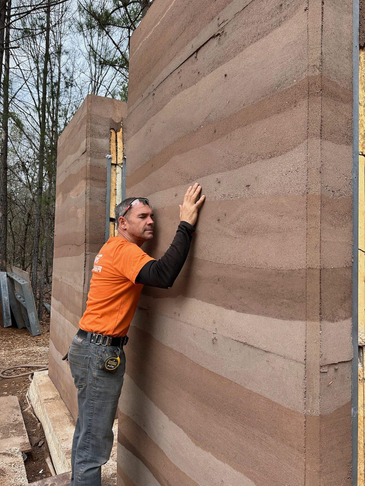 Brian Johnson with his hands on a newly stripped rammed earth wall