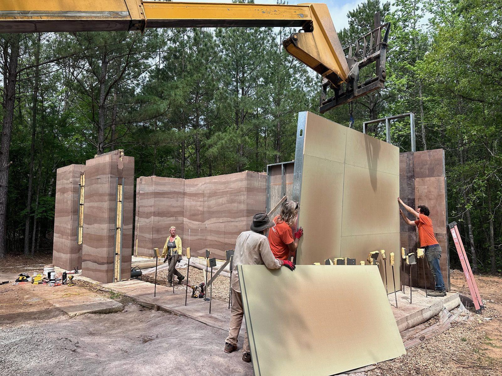 Crew guiding a formwork panel into place with a lift