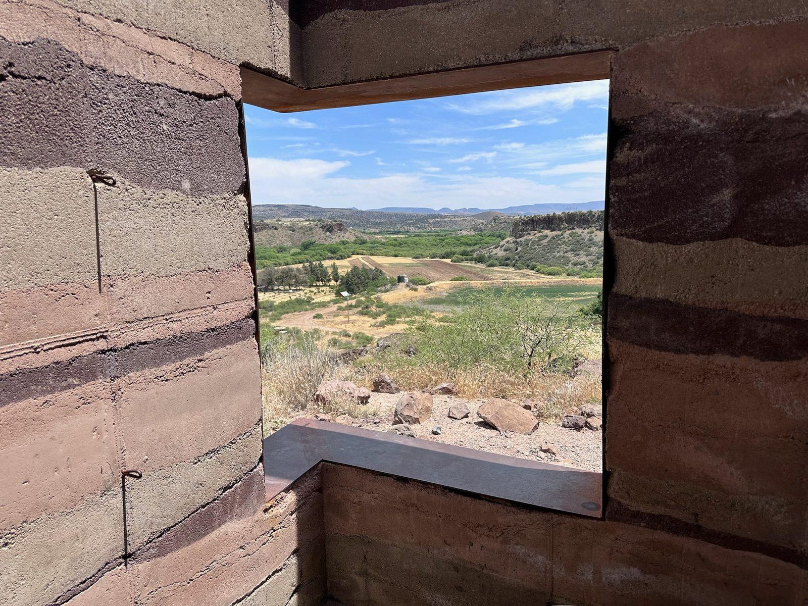 Window opening through a rammed earth wall framing the valley